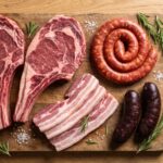 Tabla de madera con carne cruda variada para una barbacoa vista desde arriba: dos chuletones con hueso, chorizo, panceta y morcilla