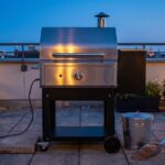Barbacoa de pellets limpia en una terraza al anochecer con un cubo metálico de cenizas al lado