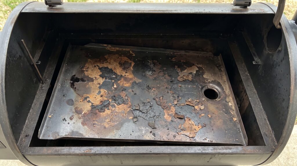 Bandeja de grasa de una barbacoa de pellets con costra de grasa quemada antes de limpiarla
